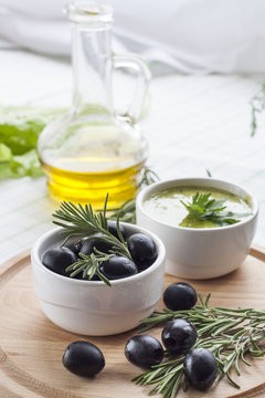 Marinated black olive and homemade sauce mayonnaise in ceramic pots. Marinated black olive and homemade sauce mayonnaise in ceramic pots with parsley, rosemary and olive oil on wooden board.