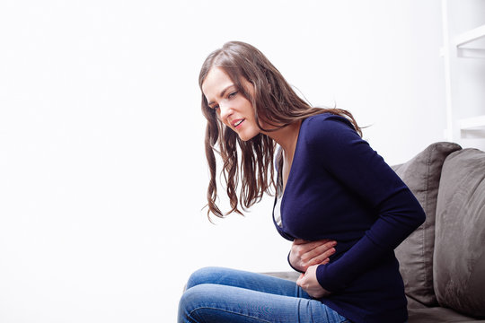  Young Woman Sitting On Sofa Suffering From stomach ache