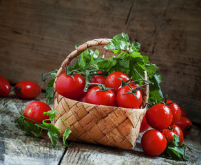 Cherry tomatoes and parsley in wicker basket on an old wooden ta