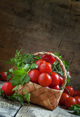 Cherry tomatoes and parsley in wicker basket on an old wooden ta