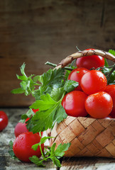 Cherry tomatoes and parsley in wicker basket on an old wooden ta