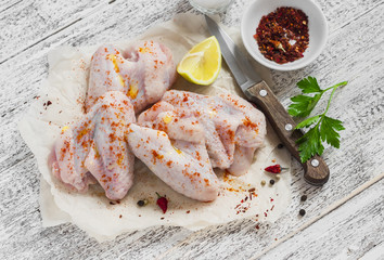 Raw ingredients to prepare spicy chicken wings, spices, salt, parsley, chicken wings on a light wooden table