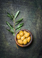 Olives in rustic bowl with oil and olive branch on dark vintage background, top view