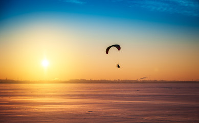 Beautiful winter sunset landscape with flying paraglider