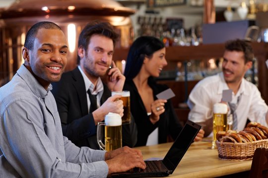 Happy office worker using laptop at bar
