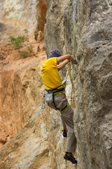 Young male climber hanging on a cliff with a rope.