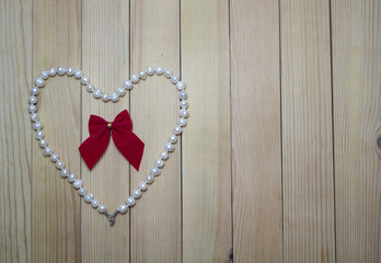 Pearl necklace with red bow in a heart on a wooden board. Love. Valentine's Day