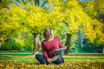 Pregnant woman reading kids book in autumn park