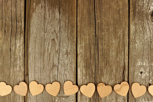 Valentines Day wooden hearts forming a bottom border on a rustic wood background
