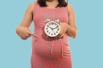 Pregnant woman holding clock. It's time. on blue background soft