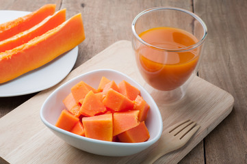 Group of orange papaya on white dish, papaya juice and wooden ba