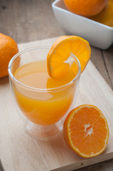 Orange juice glass on a wooden cutting board and wooden floors.