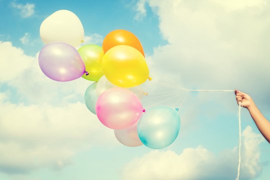 Woman hand holding colorful balloons on blue sky concept of birthday in summer and wedding honeymoon - vintage color effect