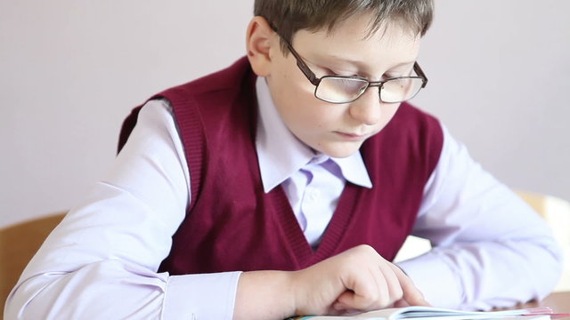 boy with glasses reading a book while sitting at a desk