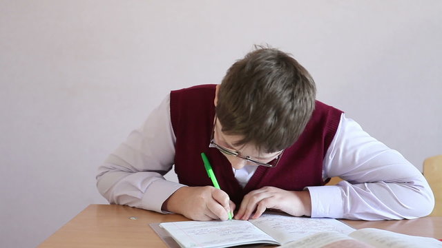 boy with glasses writes in a notebook sitting at a desk