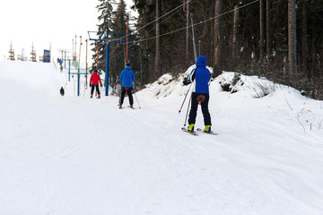Snowboarders and skiers rise on the lift up the mountain in winter frosty day