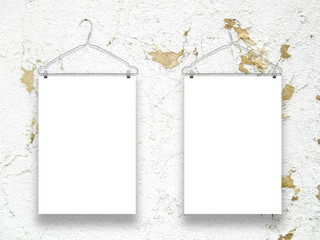 Close-up of two hanged paper sheets with clothes hangers on cracked and scratched plaster wall background