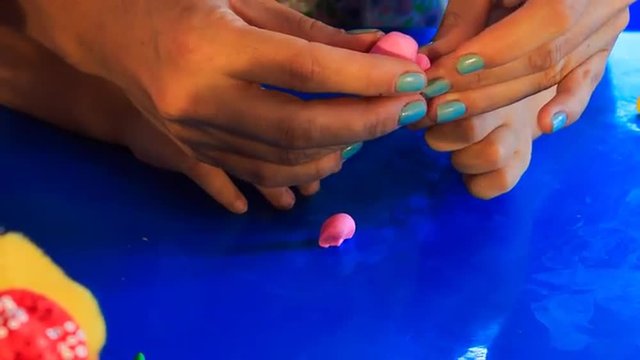mother helps kid sculpture of pink plasticine on blue table