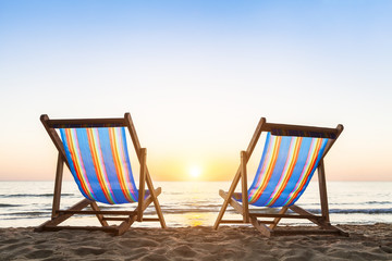 Two deck chairs on a sandy beach at sunset
