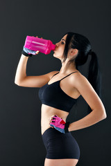 Young woman with protein shake bottle on dark background