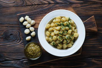 Gnocchi with pesto sauce on a rustic wooden background, top view