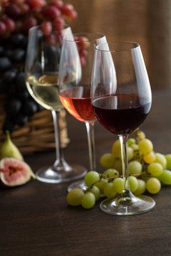 Three wineglasses of red, rose and white wine , grapes in wicker basket and figs on brown wood textured table covered with canvas towel