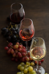 Three wineglasses of red, rose and white wine with three kinds of grapes on brown wood textured table
