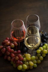 Three wineglasses of red, rose and white wine with three kinds of grapes on brown wood textured table