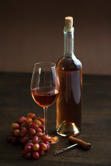wineglass with rose wine,bottle, old bottle opener and grapes on brown wood textured table