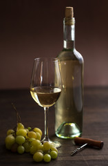 wineglass with white wine,bottle,old bottle opener and grapes on brown wood textured table