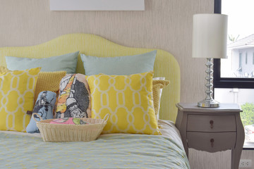 Yellow and green and pattern pillows on classic style bed and reading lamp on bedside table