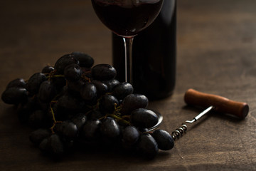 wineglass with red wine,bottle,old bottle opener and grapes on brown wood textured table
