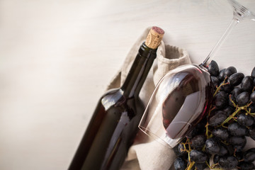wineglass with red wine with bottle and grapes on white wood textured table covered with canvas...