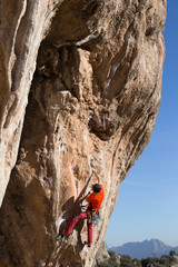 Fototapeta premium Young man climbs on a rocky wall in a valley with mountains at sunrise.