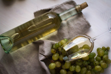 wineglass with white wine with bottle and grapes on white wood textured table covered with canvas towel