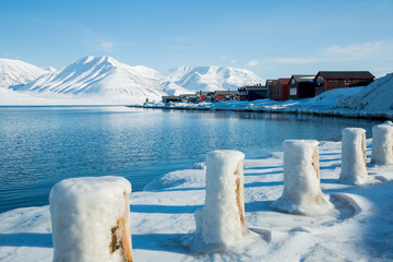 LONGYEARBYEN, SPITSBERGEN, NORWAY - APRIL 08, 2015: Small town on the shores of the Arctic ocean among snow-capped mountains of the Norwegian archipelago of Svalbard. - obrazy, fototapety, plakaty