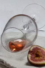 A sip of rose wine in wineglass with pink fig on canvas towel on white wood textured table