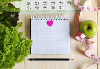 Empty notebook with vegetable salad and apple , heart, calendar on wooden table