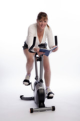 Woman working out on an exercise bike and reading a book