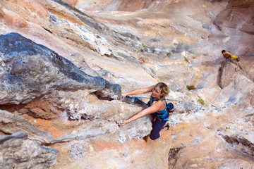 Woman Climber hanging on vertical Rocky Wall her Partner bleating and watching up