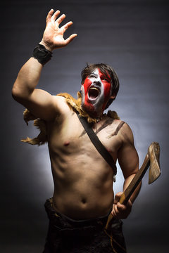 Crazy warrior in war paint with an ax in his hand stretches his hand up to the light, a savage shouts angrily