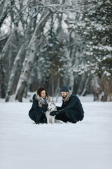 Cute young hipster couple having fun in winter park with their friend husky dog on a bright day hugging each other and smiling
