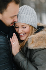 Cute young hipster couple having fun in winter park on a bright day hugging each other and smiling
