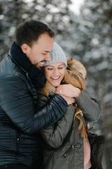 Cute young hipster couple having fun in winter park on a bright day hugging each other and smiling
