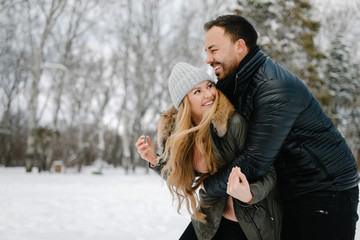 Cute young hipster couple having fun in winter park on a bright day hugging each other and smiling
