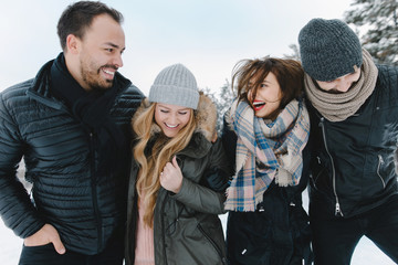 Cute young hipster couples walking in the snow having fun in winter park on a bright day hugging each other and smiling
