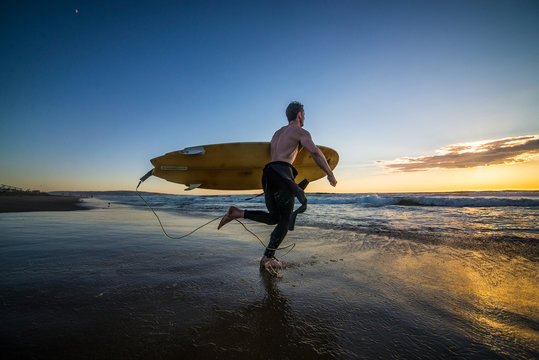 Surfer running into water with surf board at sunset
