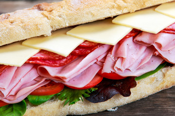 Sandwich with lettuce, slices of fresh tomatoes, salami, hum and cheese.
