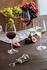 Three wineglasses of red, rose and white wine , grapes in wicker basket and figs on brown wood textured table covered with canvas towel