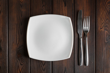 Empty plate, fork and knife on the dark wood background